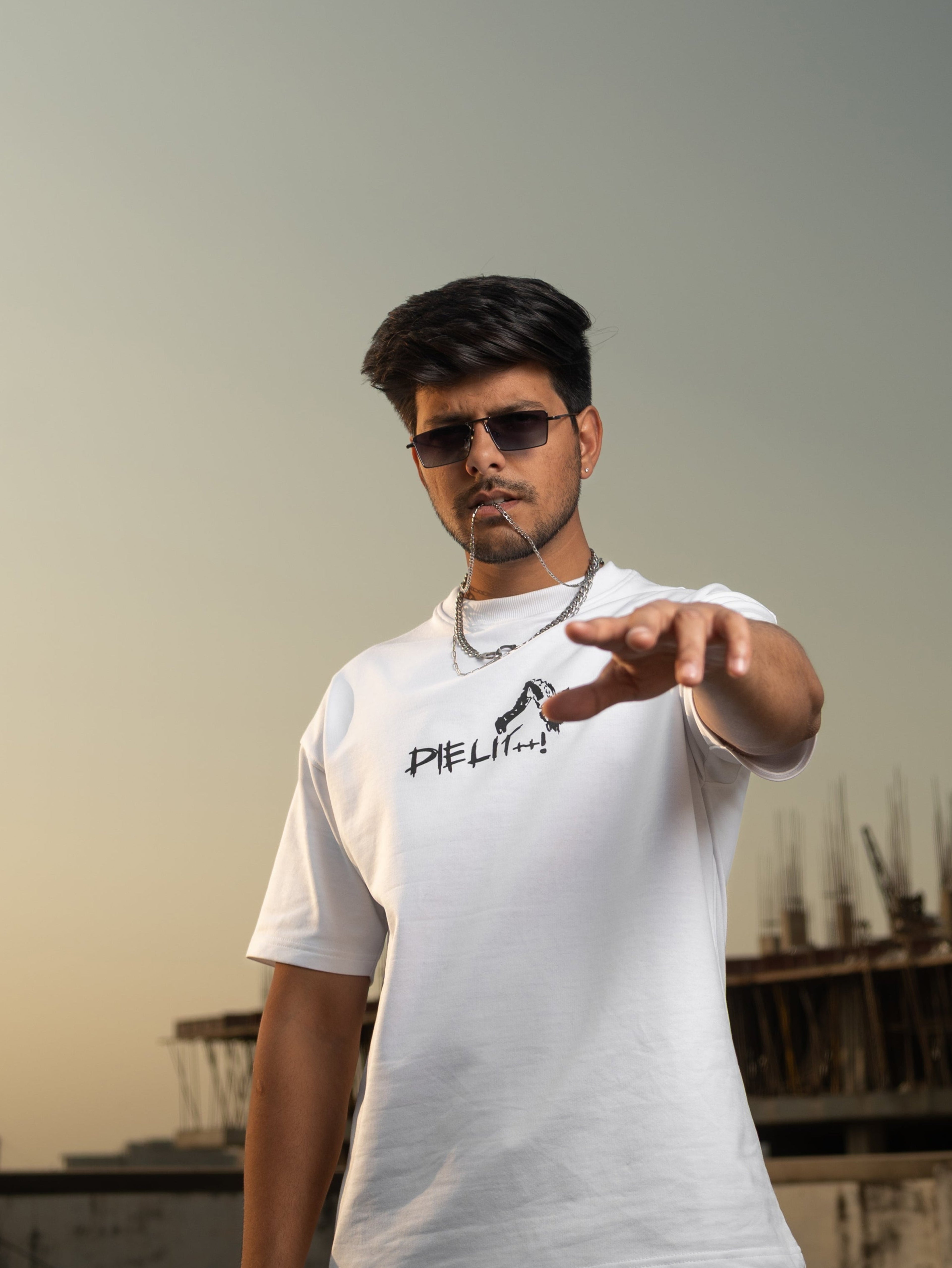 Man wearing a white t-shirt with text and black pants on a rooftop with a cityscape background.