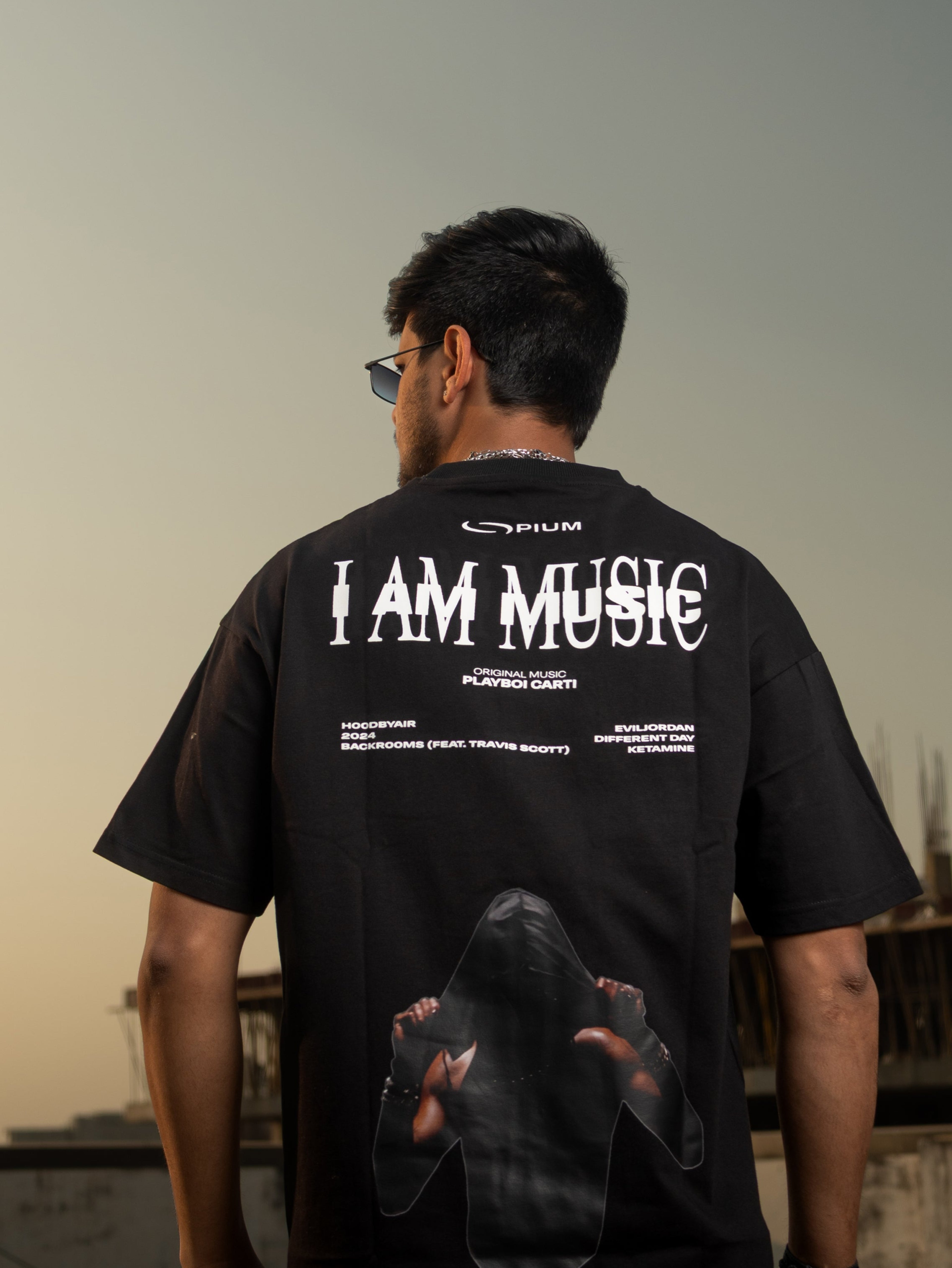 Person wearing a black t-shirt with 'I AM MUSIC' text on the back, standing on a rooftop.