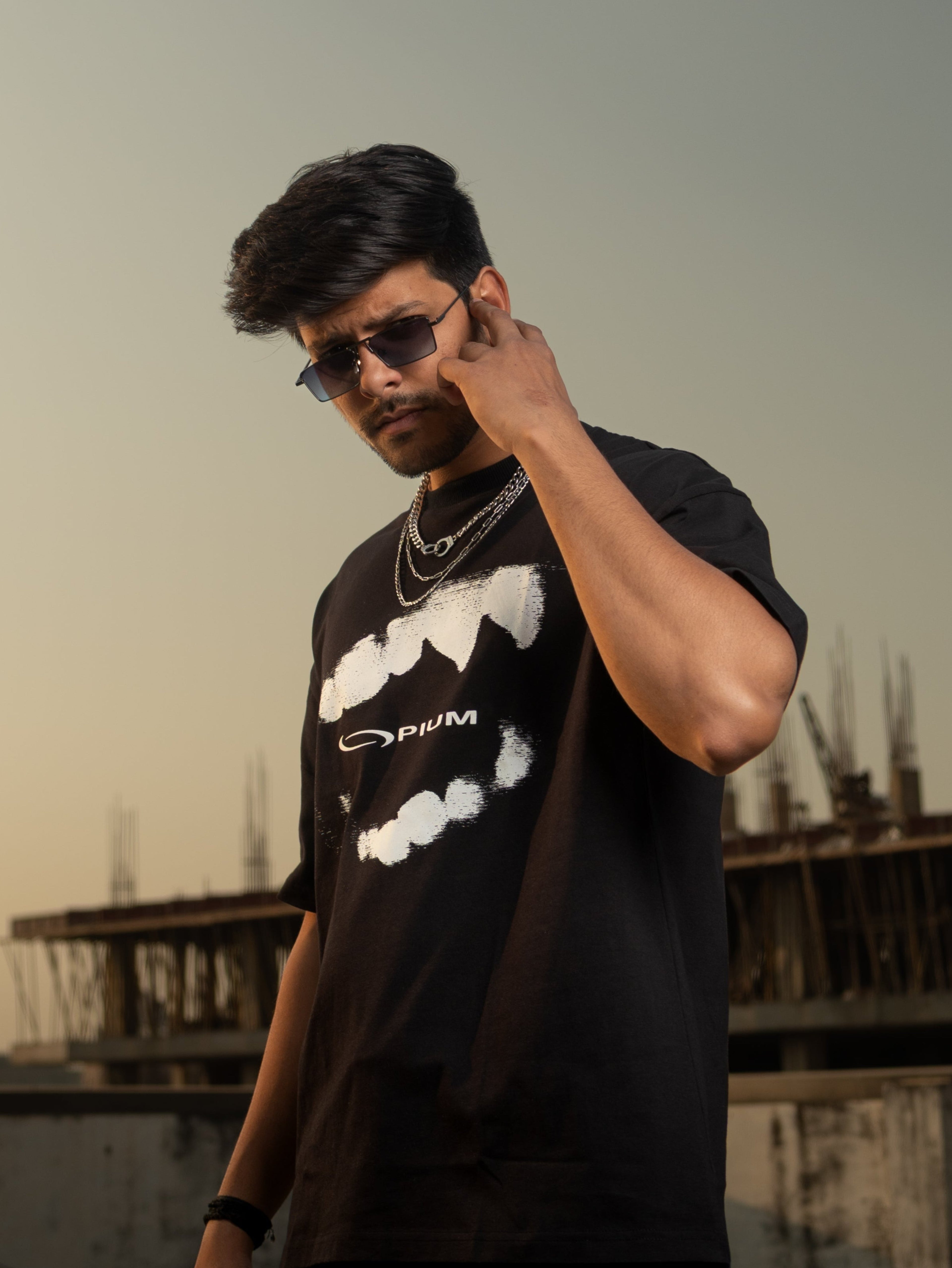 Man wearing a black t-shirt with a graphic design, standing on a rooftop with a cityscape background.