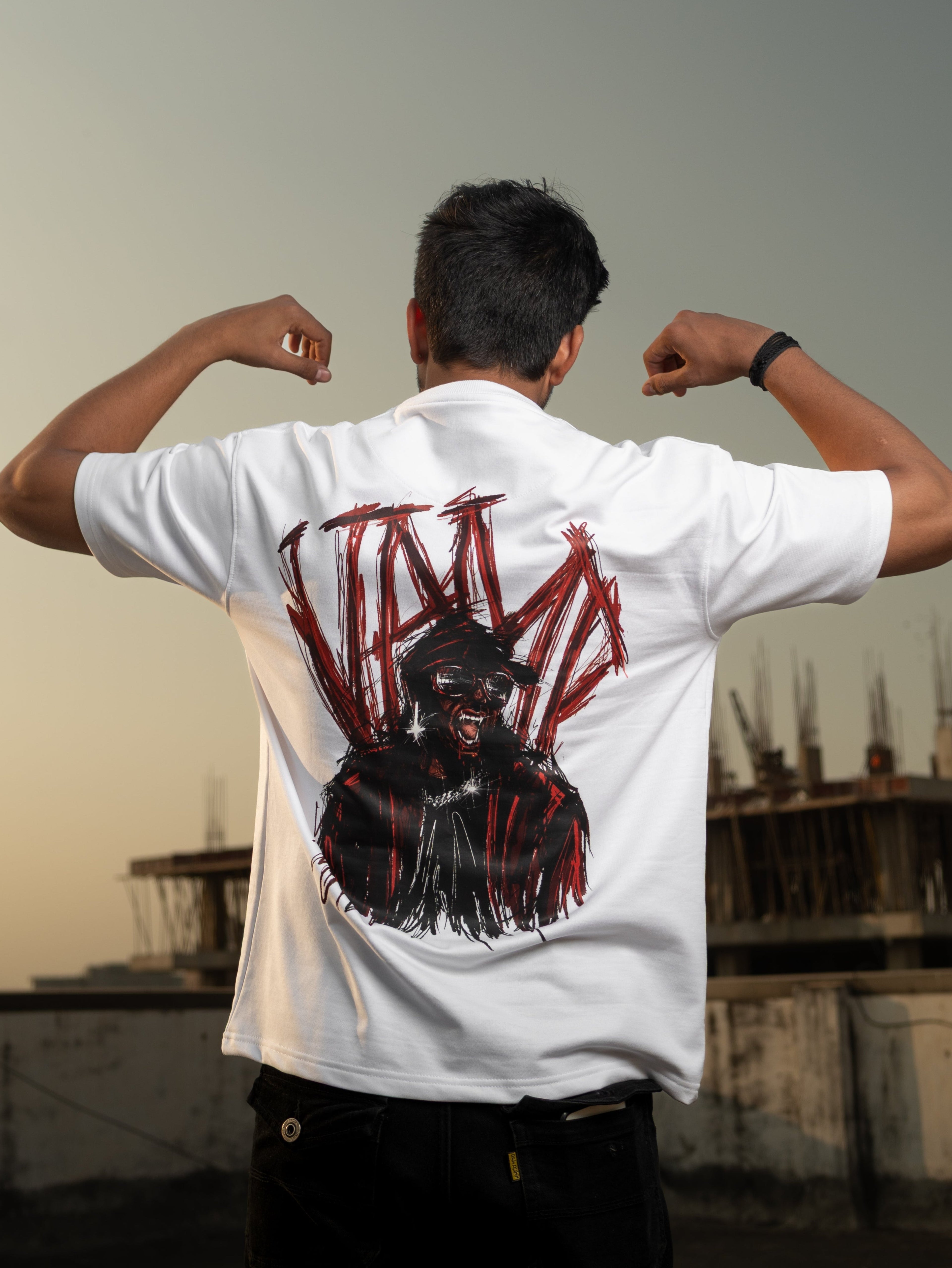 Person wearing a white t-shirt with a graphic design on the back, standing on a rooftop with a cityscape in the background.